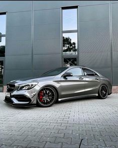 a silver mercedes benz cla parked in front of a building with two large windows