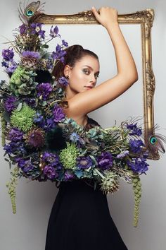 a woman in a black dress is holding a frame with purple flowers