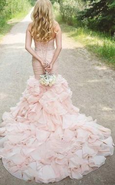 a woman in a pink dress standing on a dirt road with her back to the camera