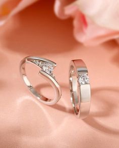 two wedding rings sitting next to each other on a pink cloth with flowers in the background