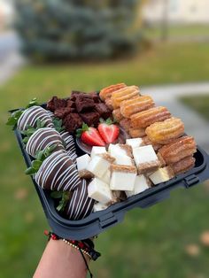 a person holding a tray with chocolate covered strawberries and pastries