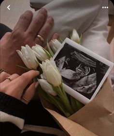 a person holding flowers in their hands and an old photo on the table next to them