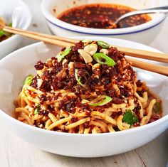 a white bowl filled with noodles and sauce next to chopsticks on a table