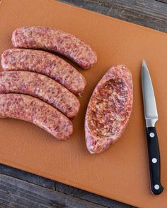 several sausages on a cutting board with a knife next to it and a piece of meat in the middle