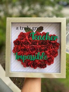 a hand holding up a framed paper cutout with the words teacher and impossible love on it