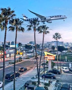 an airplane is flying over the city with palm trees and cars parked on the street