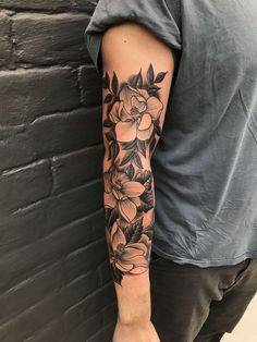 a man's arm with flowers and leaves on it, in front of a brick wall