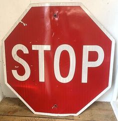 a red stop sign sitting on top of a wooden floor next to a white wall