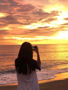 a woman standing on top of a beach holding a cell phone up to her face