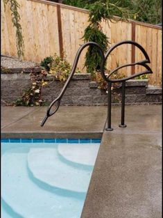 an empty swimming pool with a metal handrail next to it and a wooden fence in the background