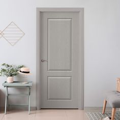 an empty room with a gray door and grey chair next to the table on which there is a potted plant