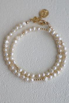 This is not your average pearl bracelet... Our Pearl Double Wrap Bracelet with white pearls features a double wrap style with with gold beaded accents. Wear solo or stacked with your favorite pieces! Materials: Medium pearls and gold filled beads with a gold plated coin ending. Length: Measures an adjustable 14-15" with an inch and a half extender Classic White Pearl Bracelet With Gold Beads, Gold Pearl Single Strand Beaded Bracelets, Adjustable White Pearl Necklace With 14k Gold Filled, Adjustable White Pearl Necklace In 14k Gold Filled, Adjustable Double Strand Gold Pearl Necklace, Gold Single Strand Pearl Bracelet With Round Beads, Gold Pearl Bracelet With Single Strand Of Round Beads, Everyday Gold Single Strand Pearl Bracelet, White Pearl Chain Bracelet In 14k Gold Filled