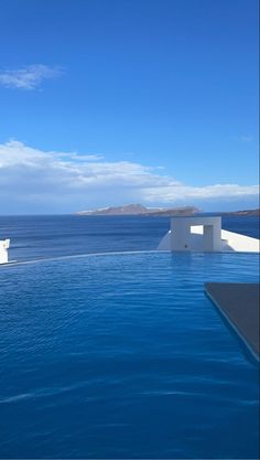 an empty swimming pool next to the ocean with two white structures in the water and one large body of water