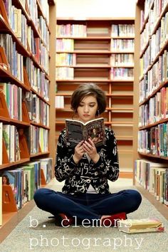 a woman is sitting on the floor in front of bookshelves and reading a book