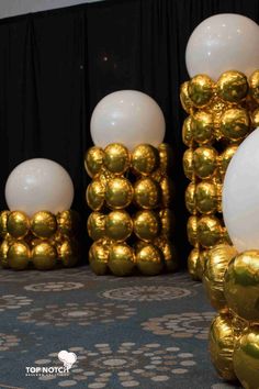 gold and white balloons are stacked on top of each other in front of a black backdrop