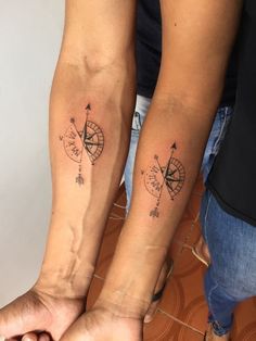 two people holding hands with tattoos on their arms and both have compasss tattooed on them