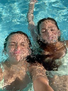 two people swimming in a pool with their arms around each other and water splashing all over them