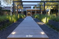 a wooden walkway leading to a building surrounded by trees and plants at night with lights on