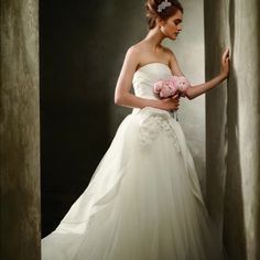 a woman in a white wedding dress holding a pink flower and posing for the camera