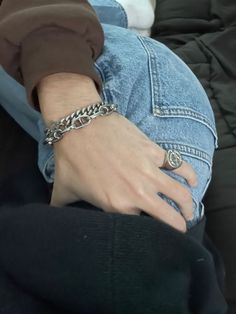 a person wearing a chain bracelet on their arm and sitting in the lap of someone's jeans