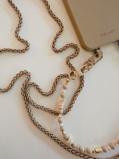 a cell phone is connected to a necklace with pearls and other beads on it's side