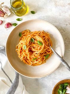 a white bowl filled with pasta next to two bowls of olive oil and garlic florets