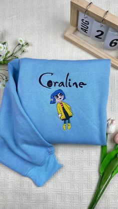 a blue bag with the name coraline on it next to flowers and a clock