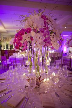 the table is set with wine glasses, napkins and flowers in tall vases