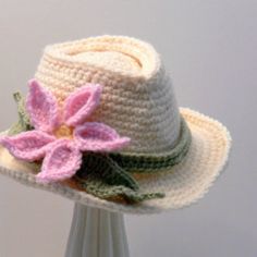 a white crocheted hat with pink flower on the brim and green band