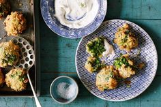 two plates with food on them next to a bowl of ranch dressing and a pan of broccoli florets