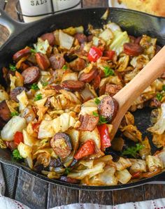 a skillet filled with sausage, onions and peppers next to a bottle of wine