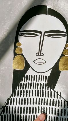 a woman's face is drawn on a piece of paper with gold ear rings