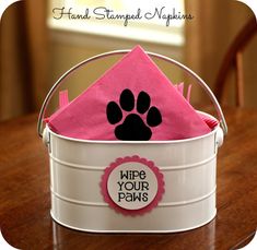 a white bucket with pink napkins and a black paw print on the top that says wipe your paws