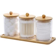 three canisters with wooden lids and white cotton balls in them on a wood tray