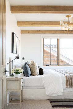 a white bed sitting under a window next to a wooden ceiling mounted light above it