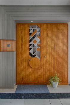 a wooden door with an abstract design on the side and plant in front of it