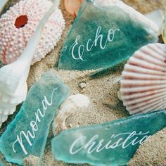 sea glass with names on them sitting in the sand next to shells and seashells