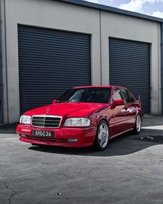 a red mercedes benz parked in front of a garage with roller doors on the side