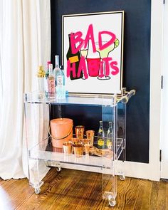 a clear bar cart with bottles and glasses on it in front of a black wall