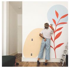 a woman is painting a wall with red and blue leaves on it in an apartment