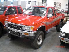 two red pick up trucks parked in a showroom next to other vehicles on display