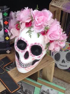 a white skull with pink flowers on it's head sitting next to other skulls