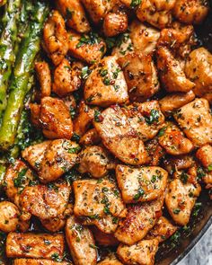 chicken and asparagus in a skillet on a marble surface with a wooden spoon