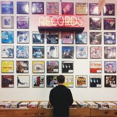 a man sitting on a bench in front of a wall covered with records and posters