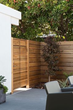 an outdoor patio area with chairs and wooden privacy fence in the background, surrounded by greenery