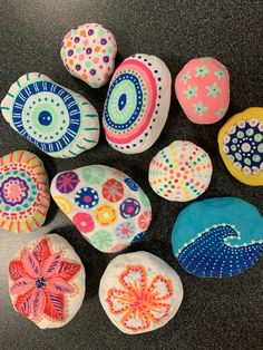 painted rocks are arranged in the shape of flowers and paisleys on a black surface