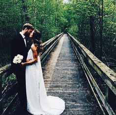 two people standing on a bridge with trees in the background and one person holding a bouquet