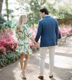 a man and woman holding hands while walking down a path with flowers in the background