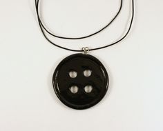 a black button is hanging from a cord on a white surface with two holes in the middle