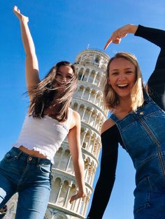 two young women standing next to each other in front of a tall building with a tower